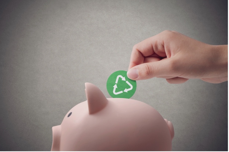 A hand putting a green recycle coin into a piggy bank