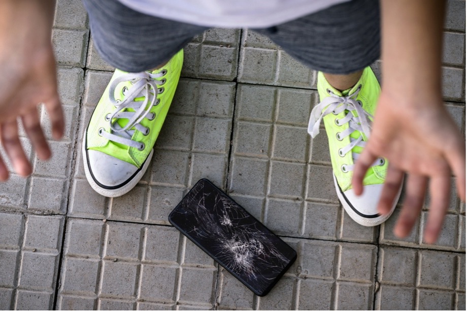 A person in yellow sneakers next to a broken phone