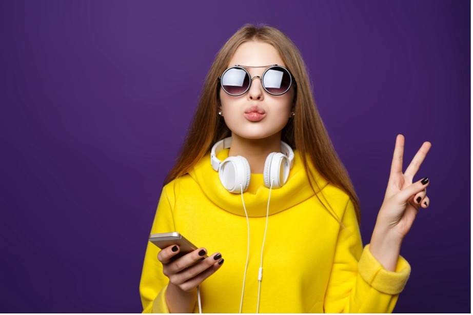 A person wearing sunglasses and a yellow hoodie holding a phone and a purple background